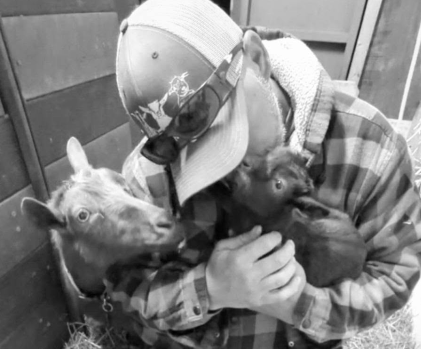 Justin holding two young goats close in a barn.