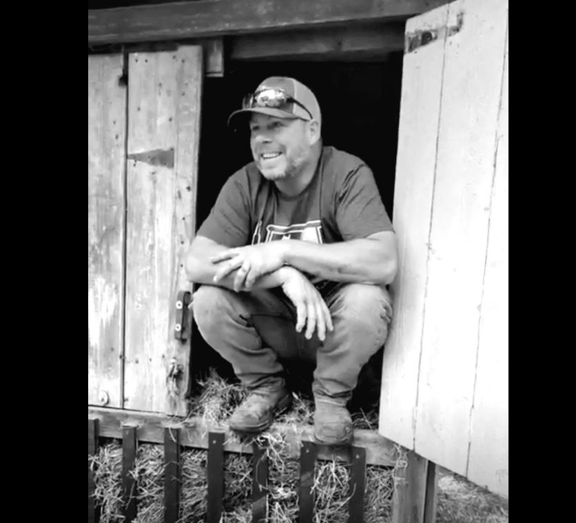 Justin smiling while seated in an open barn doorway.