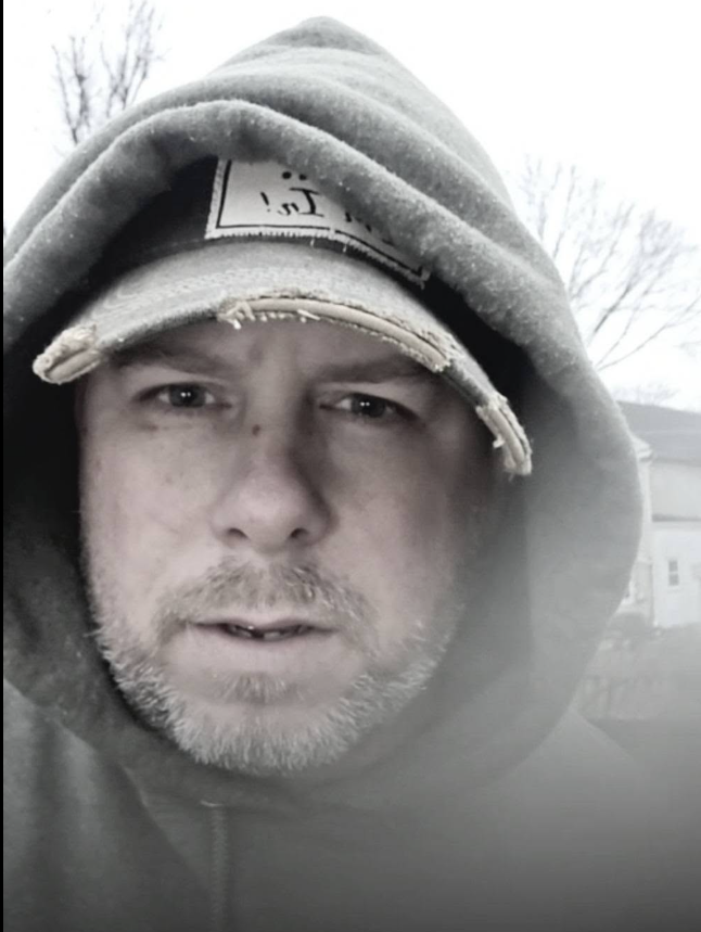 Close portrait of Justin in a hood and worn baseball cap.
