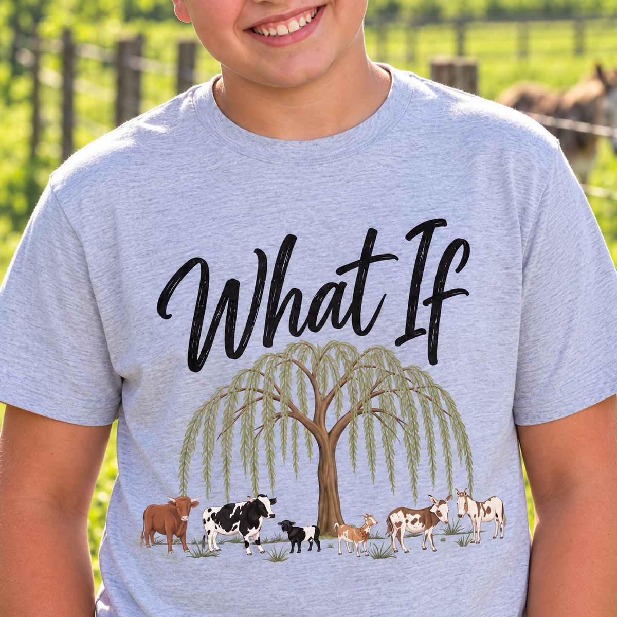 Close-up of the What If lettering, willow tree and farm animals on Jayden's grey shirt at the farm.